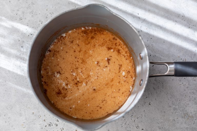 A saucepan containing ingredients for apple cinnamon oatmeal with specks of cinnamon on a light gray countertop.