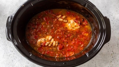 Chicken breasts, beans, diced tomatoes, and spices in a slow cooker with broth, ready to be cooked.