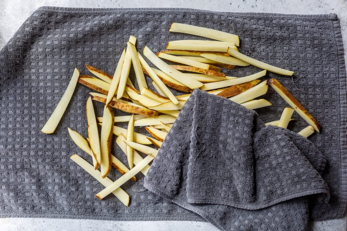 Raw potato fries are spread out on a gray towel, some partially covered by another section of the towel.