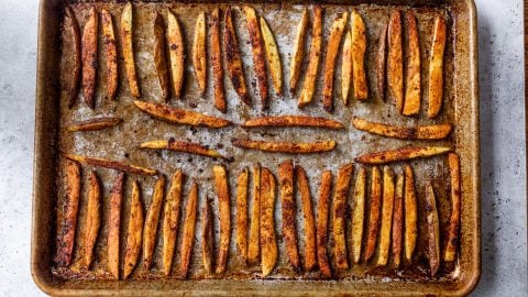 A baking sheet with rows of seasoned, baked potato fries on a light-colored surface.
