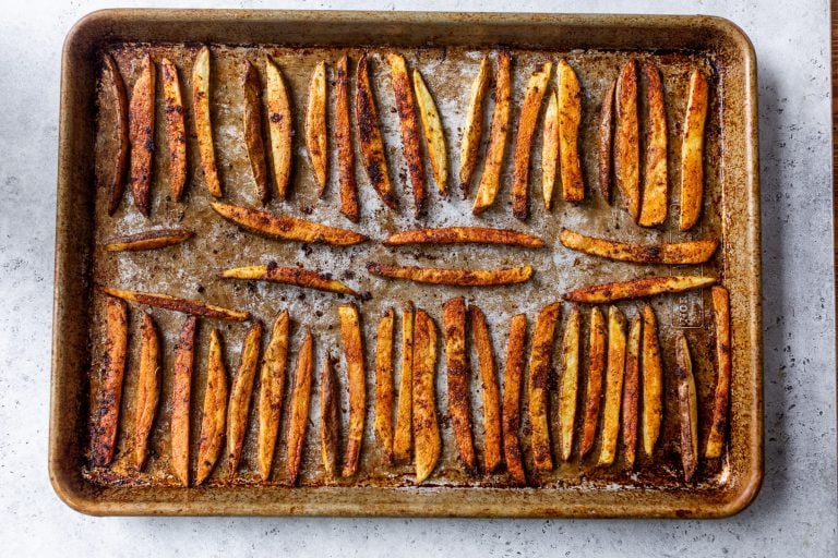 A baking sheet with rows of seasoned, baked potato fries on a light-colored surface.
