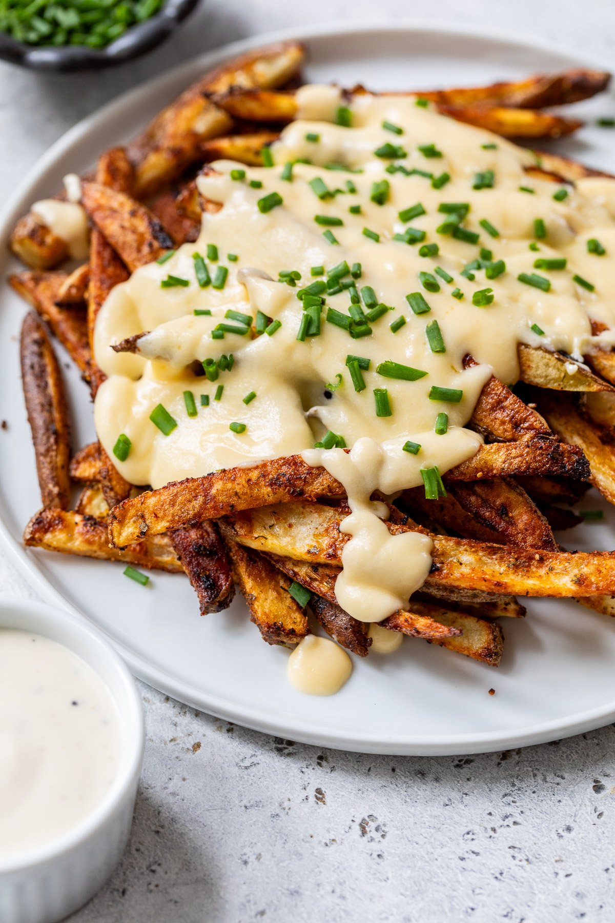 A plate of seasoned voodoo fries topped with melted cheese sauce and chopped chives, with a side of dipping sauce.