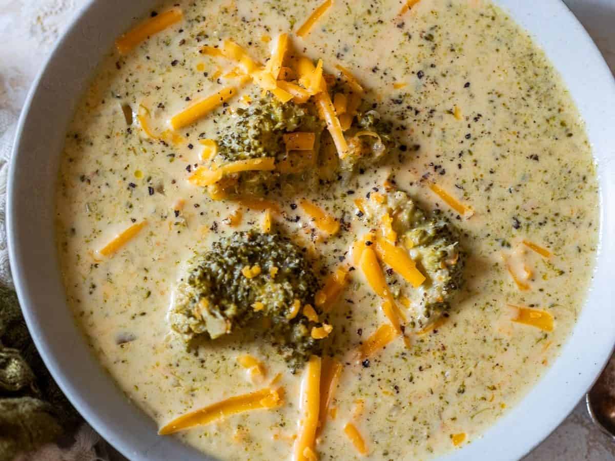 Crockpot broccoli cheese soup in bowl with shredded cheese for garnish.