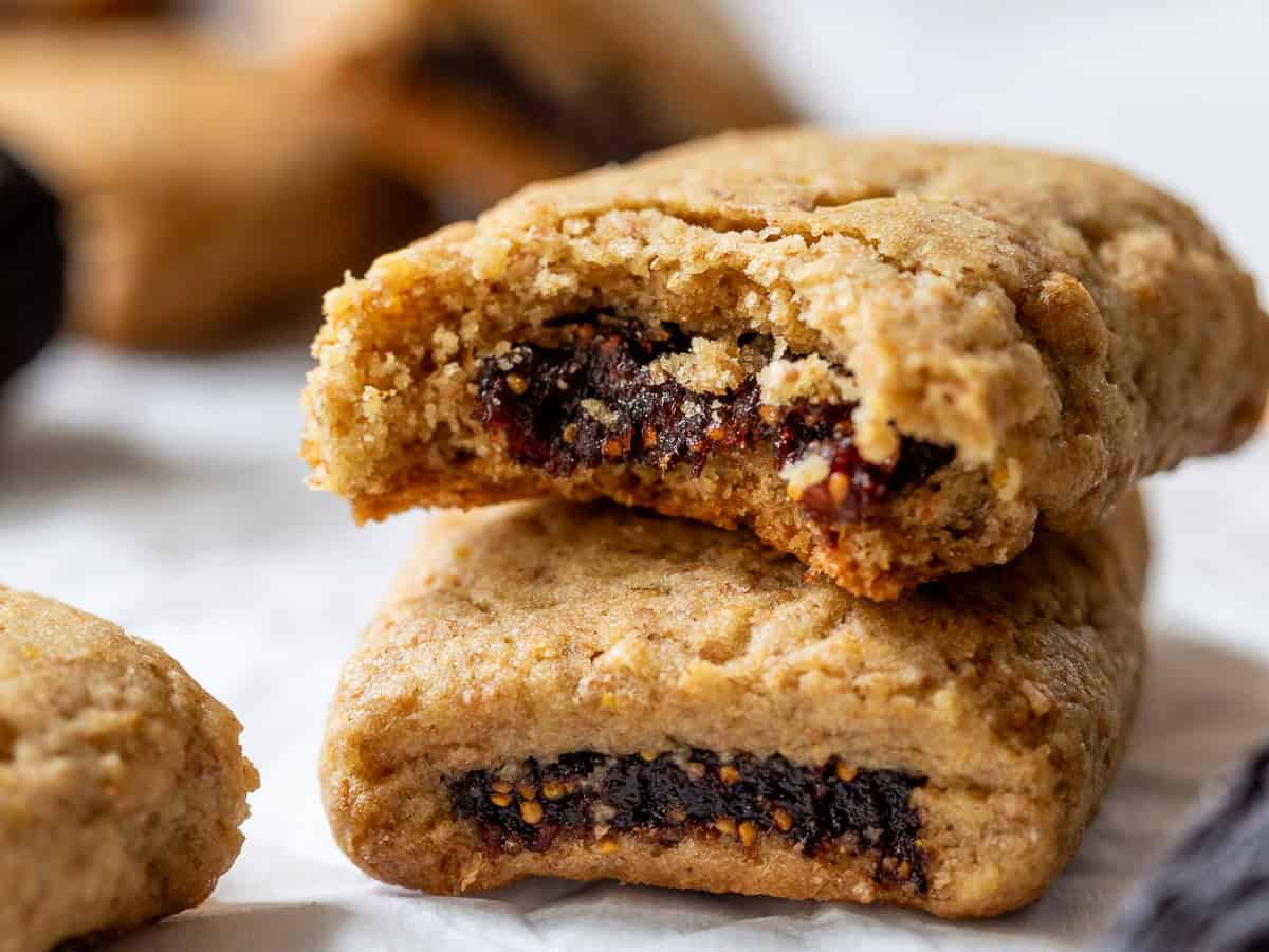 Two fig bars, one stacked on top of the other, with the top cookie showing a bite and fig filling inside.