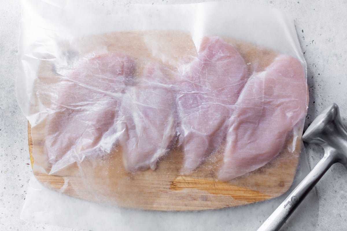 Chicken cutlets on cutting board with parchment paper on top.