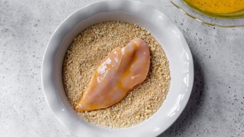 Chicken cutlet in bowl of breadcrumbs.