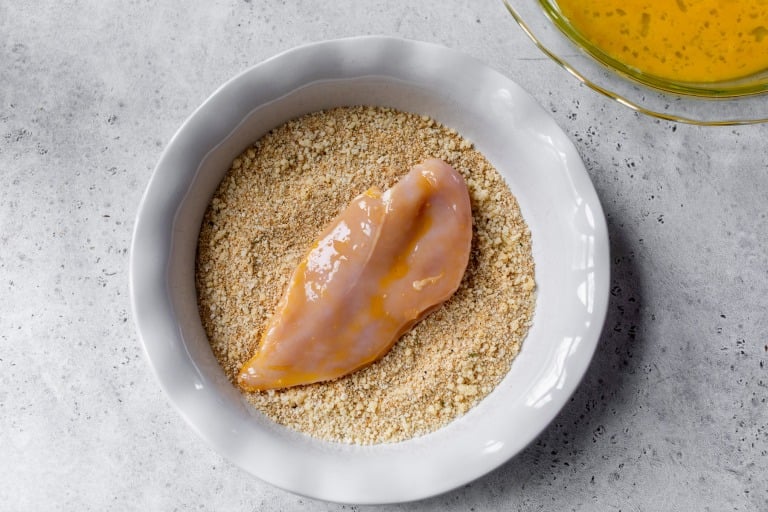 Chicken cutlet in bowl of breadcrumbs.