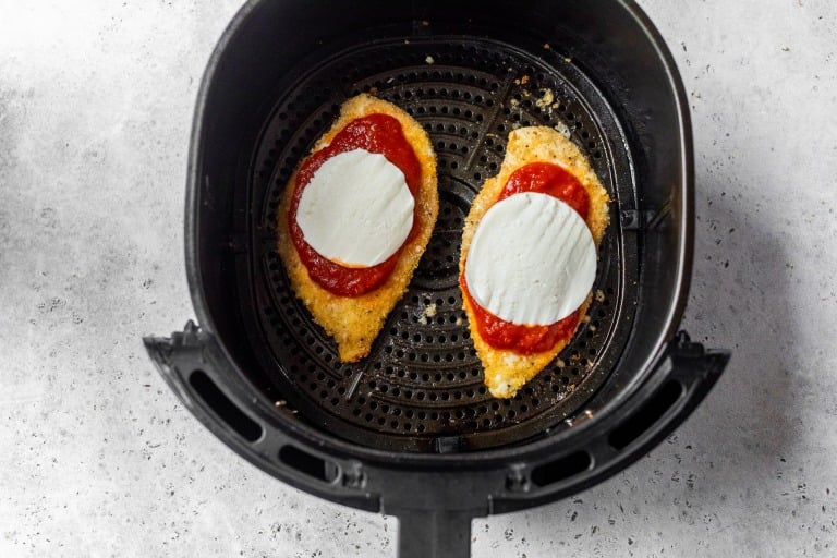 Marinara and mozzarella added to chicken Parmesan in air fryer.