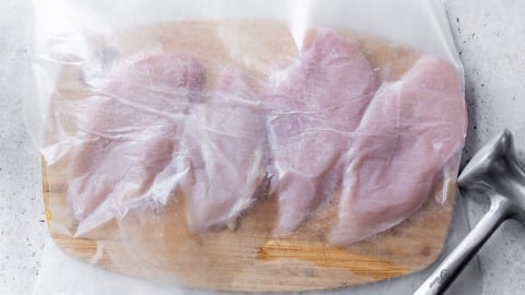 Chicken cutlets on cutting board with parchment paper on top.