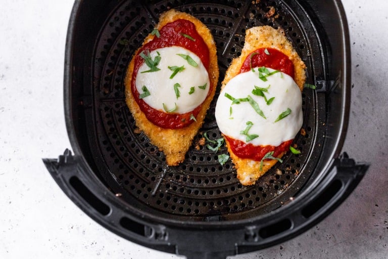 Chicken Parmesan in air fryer topped with basil.