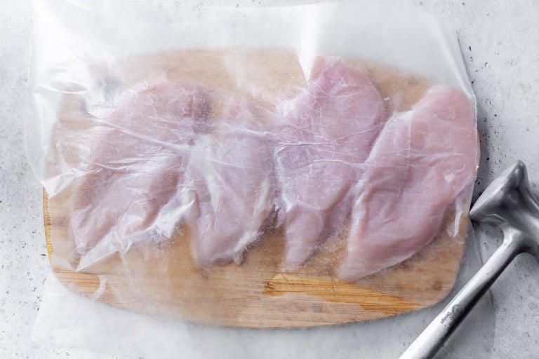 Chicken cutlets on cutting board with parchment paper on top.