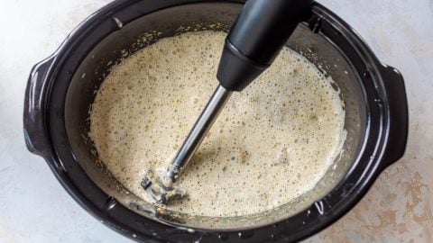 Immersion blender pureeing broccoli cheese soup in crockpot.