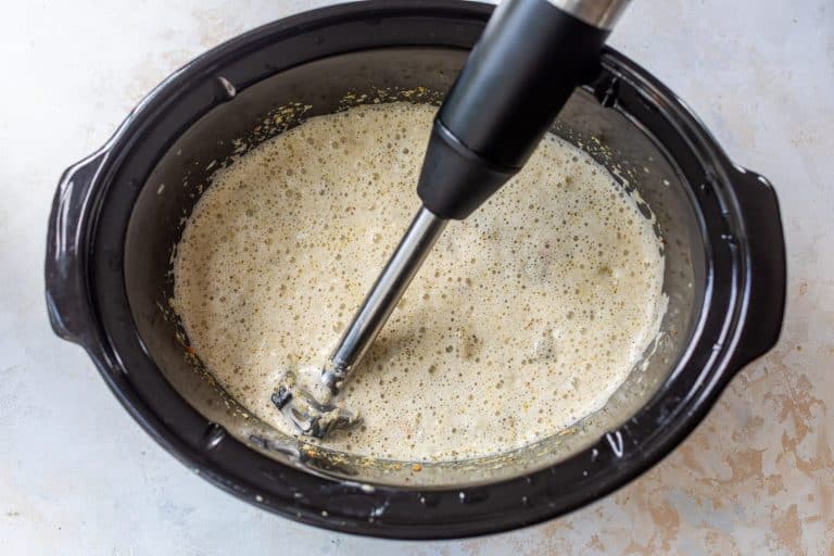 Immersion blender pureeing broccoli cheese soup in crockpot.