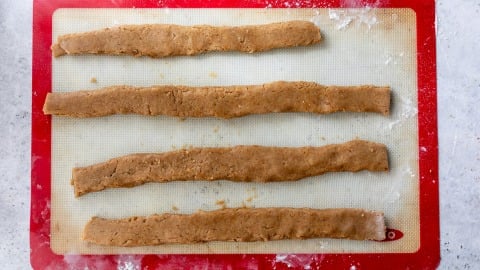 Four unbaked fig bar dough strips on a silicone baking mat placed on a lightly floured surface.