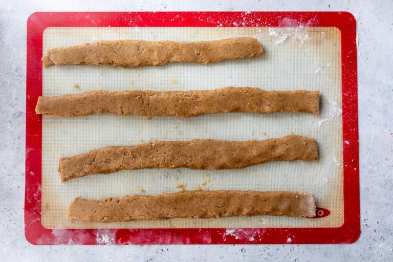 Four unbaked fig bar dough strips on a silicone baking mat placed on a lightly floured surface.