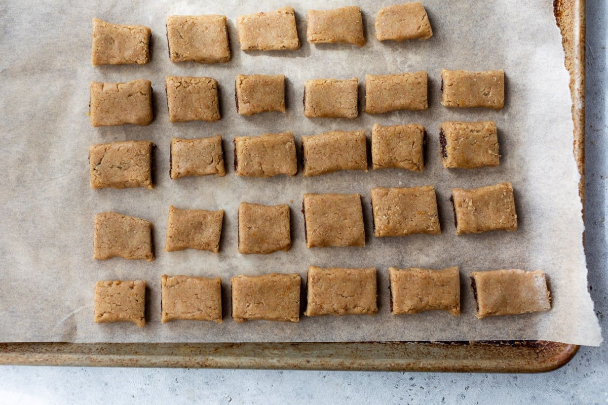 Rectangular fig bars spaced evenly on parchment paper on a baking sheet, ready to be baked.