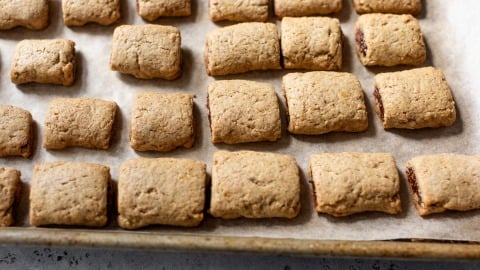 Rectangular fig bars arranged on a parchment-lined baking sheet.