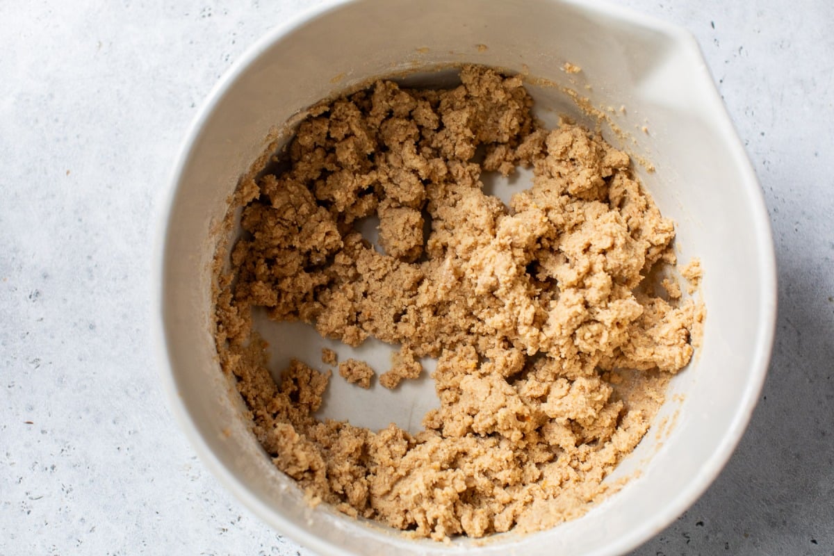 A mixing bowl filled with coarse, light brown fig bar dough on a gray surface.