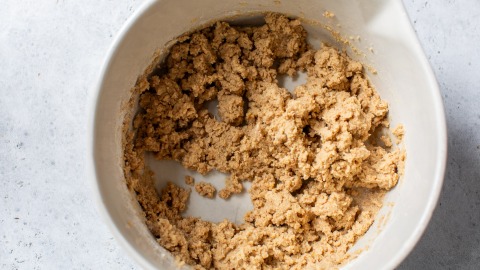 A mixing bowl filled with coarse, light brown fig bar dough on a gray surface.