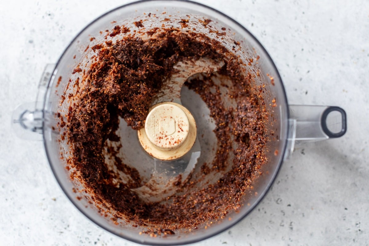 Blended fig paste in a food processor bowl on a light gray surface, viewed from above.