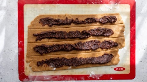 Dough strips on a silicone mat topped with a thick, dark fig filling, ready to be rolled or folded.