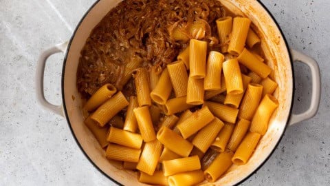 Rigatoni added to caramelized onions in Dutch oven.