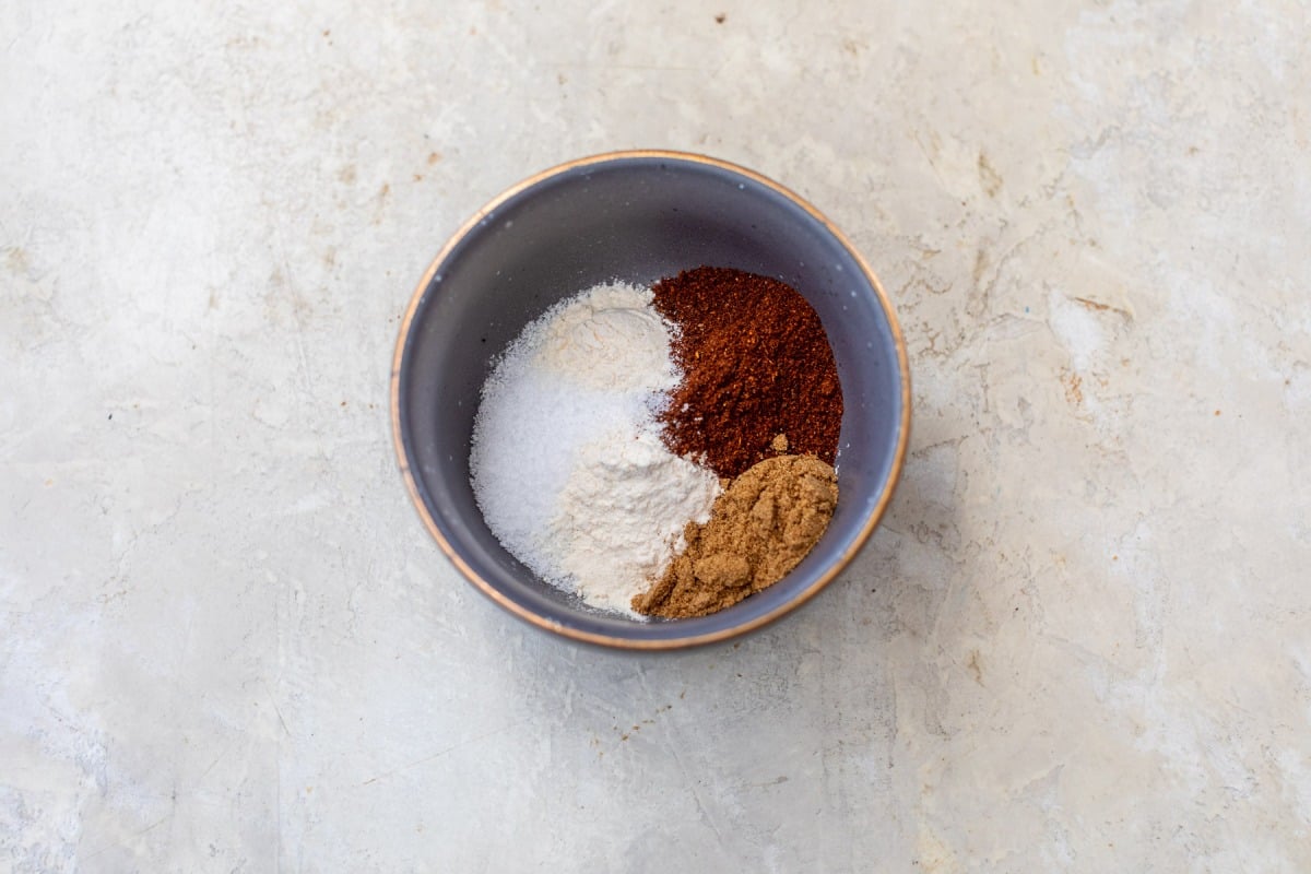 A bowl containing four different spices and seasonings for chicken fajitas on a light, textured surface.