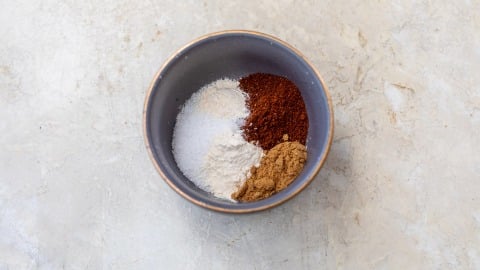 A bowl containing four different spices and seasonings for chicken fajitas on a light, textured surface.