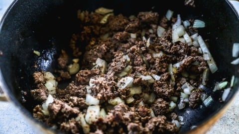 Ground beef and chopped onions cooking together in a black skillet.