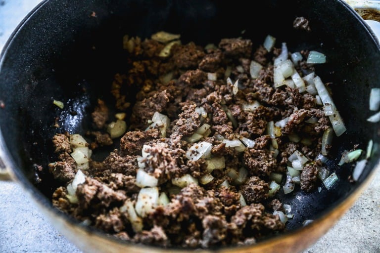 Ground beef and chopped onions cooking together in a black skillet.