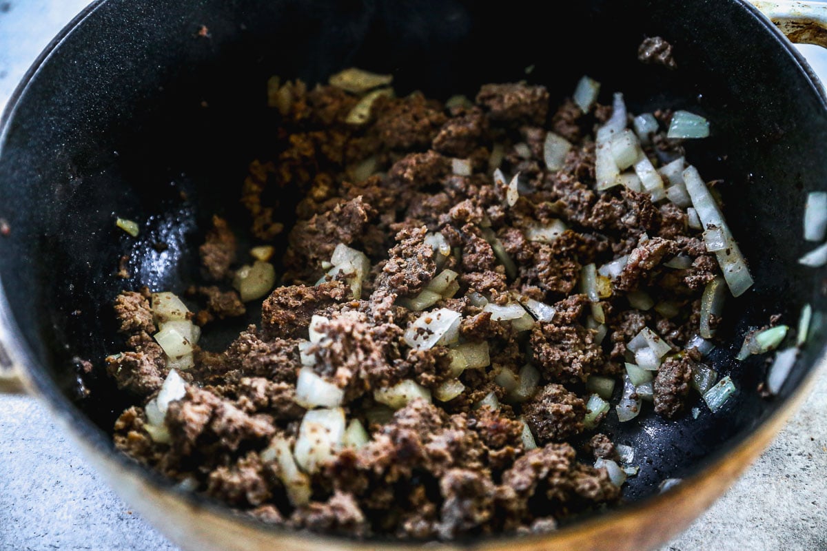 Ground beef and chopped onions cooking together in a black skillet.