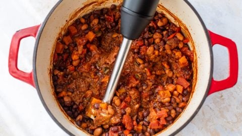 Immersion blender pureeing vegan chili in Dutch oven.