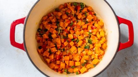 Sweet potatoes, red and green bell peppers, and onions in Dutch oven.
