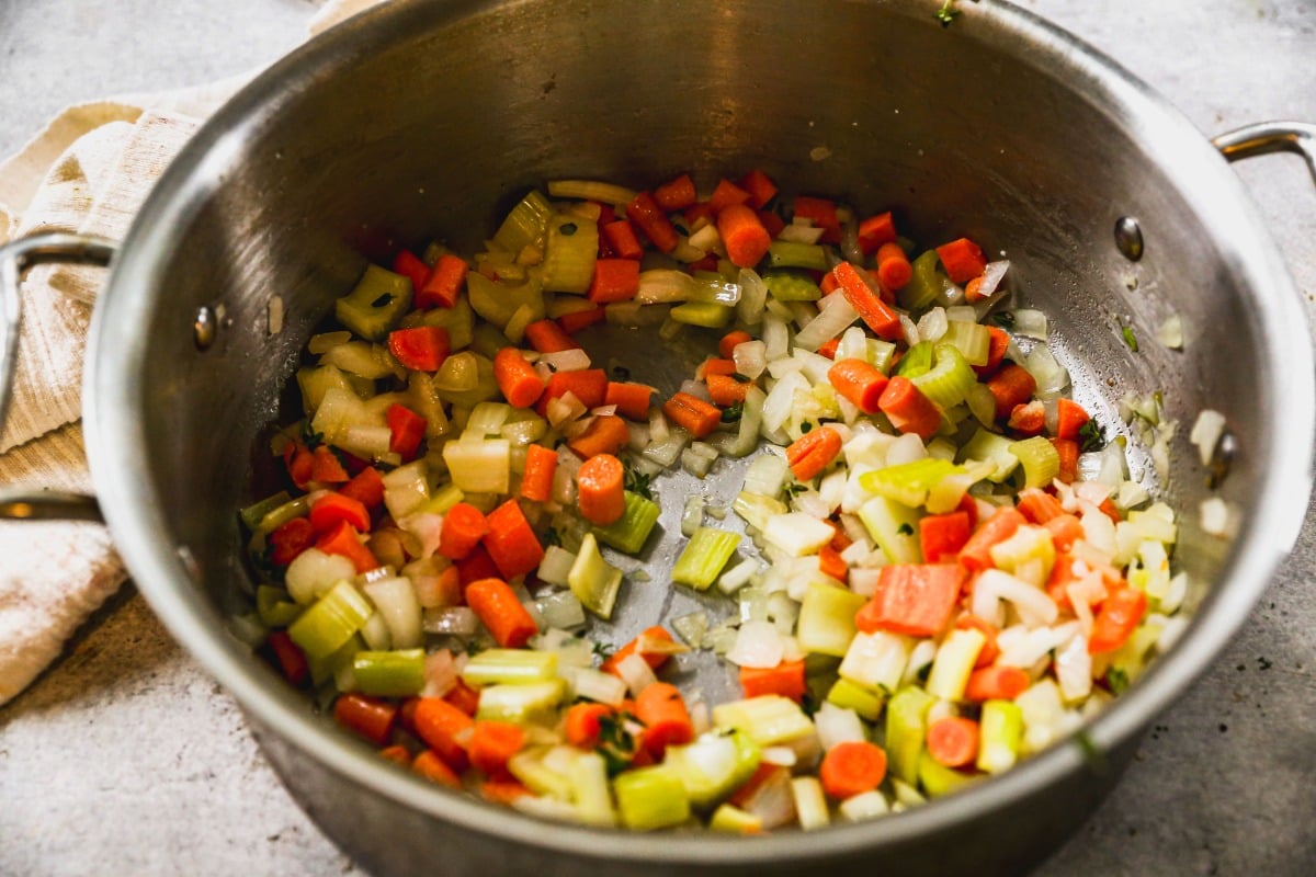 Chopped carrots, celery, and onions sautéing in a large metal pot.
