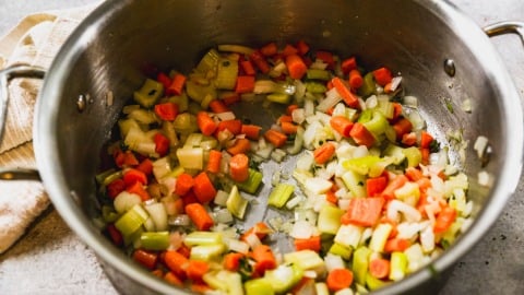 Chopped carrots, celery, and onions sautéing in a large metal pot.