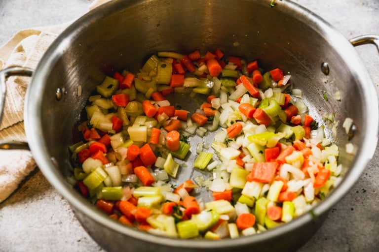 Chopped carrots, celery, and onions sautéing in a large metal pot.