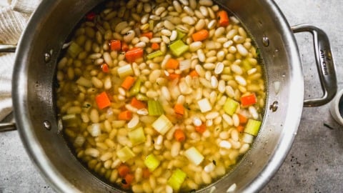 A pot of white bean soup with diced carrots and celery in a clear broth, viewed from above.