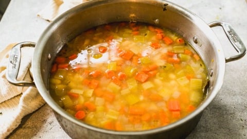 A pot of homemade white bean soup with carrots, celery, and onions simmering in broth.