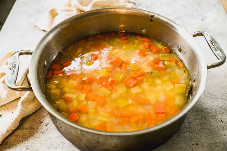 A pot of homemade white bean soup with carrots, celery, and onions simmering in broth.