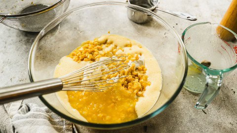 Whisk in glass bowl with corn souffle ingredients.