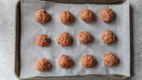 Unbaked pork meatballs on parchment lined sheet pan.