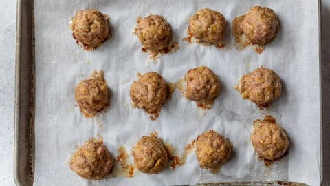 Baked pork meatballs on parchment-lined sheet pan.