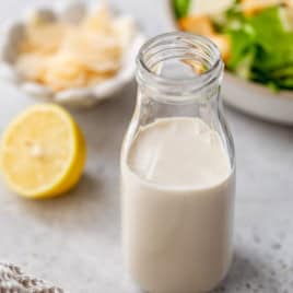 Homemade Caesar dressing in bottle with salad in background.