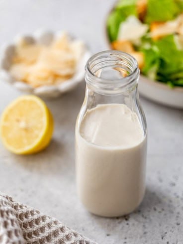 Homemade Caesar dressing in bottle with salad in background.