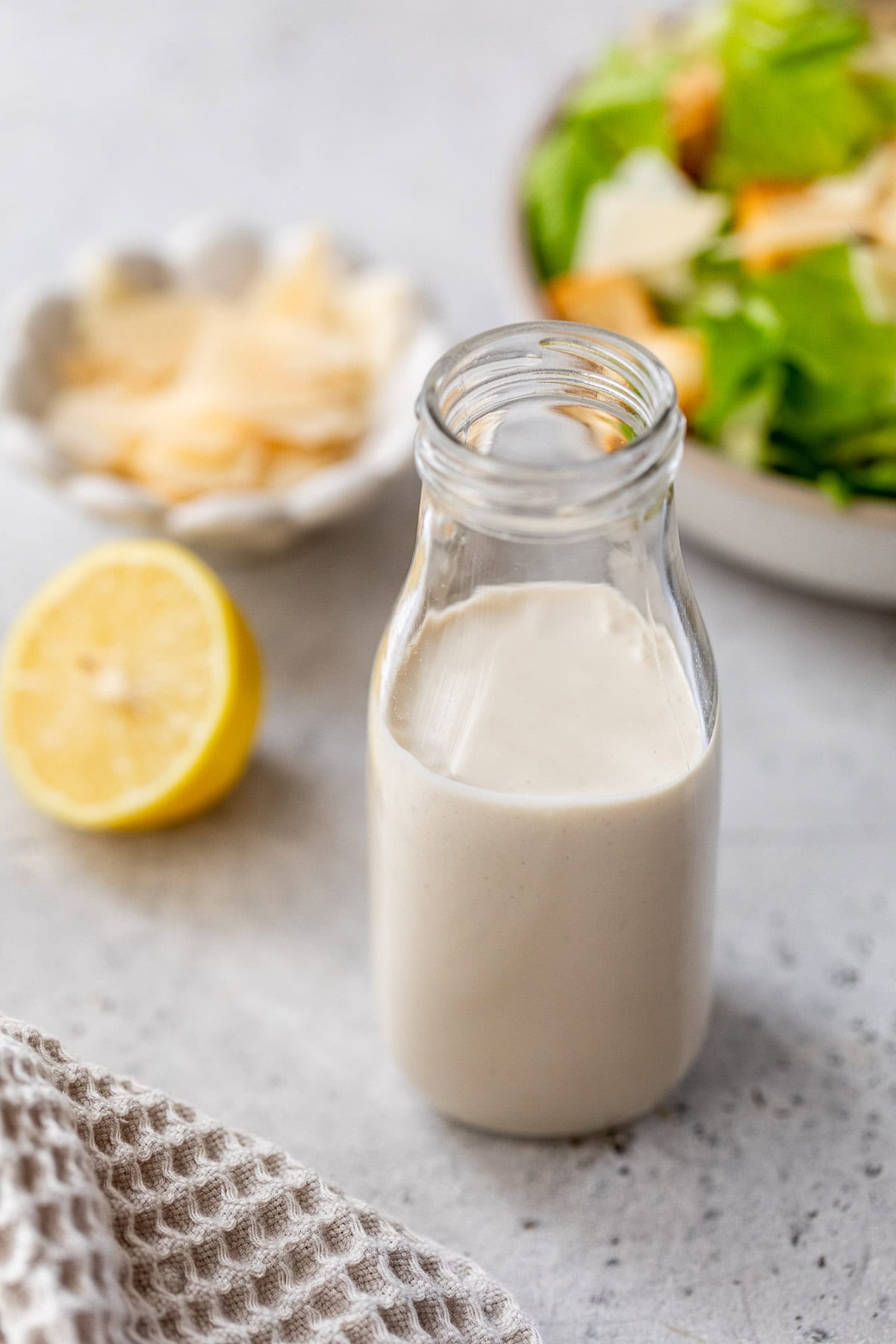 Homemade Caesar dressing in bottle with salad in background.