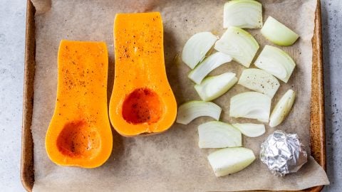 Halved butternut squash, onions, and foil-wrapped garlic on pan before baking.