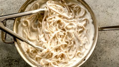 Tongs combining fettuccine with cottage cheese alfredo sauce.