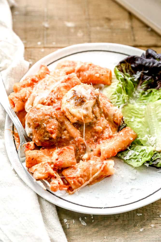 A plate of meatball casserole with tomato sauce, melted cheese, meatballs, and a small side of leafy green lettuce.