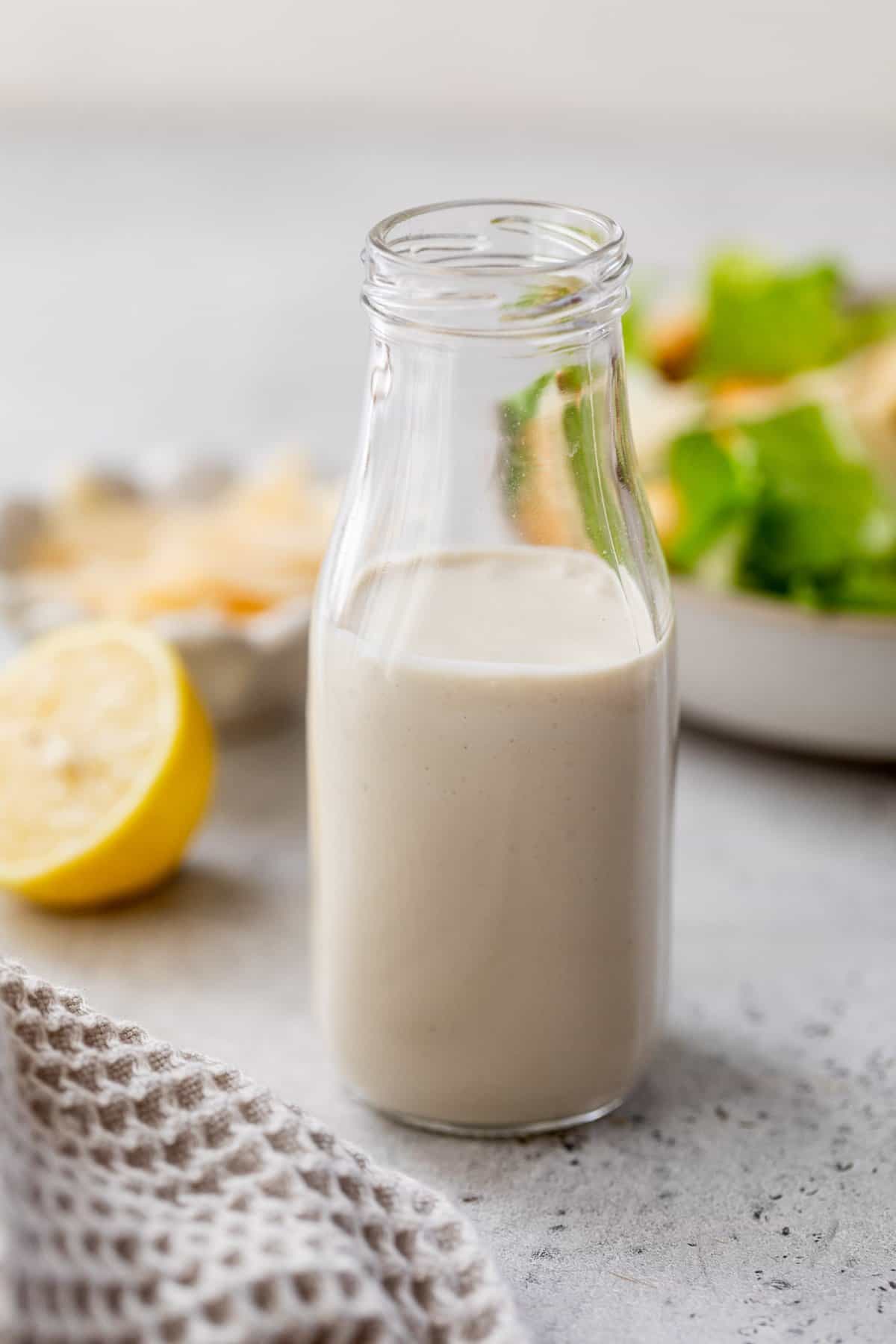 Healthy Caesar dressing in bottle with salad in background.
