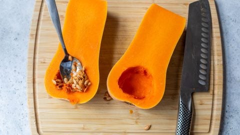 Spoon scooping seeds from halved butternut squash.